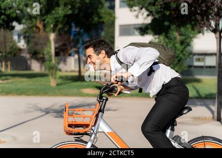 Cheerful businessman with backpack riding electric bicycle in city Stock Photo