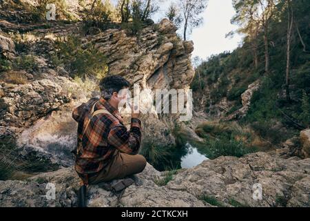 Bushcrafter smoking pipe while sitting on rock formation Stock Photo
