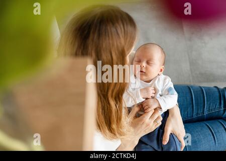 Blond woman holding sleeping baby boy in arms while sitting on floor at home Stock Photo
