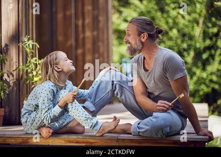 Father and daughter showing teeth to each other while sitting in yard Stock Photo
