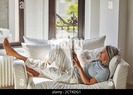 Woman reading magazine while lying on sofa at home Stock Photo