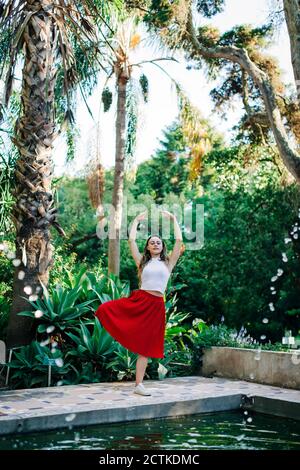 Young woman with arms raised dancing on footpath against trees in park Stock Photo