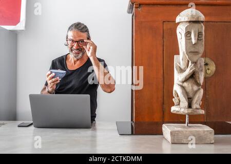 Smiling man with bowl using laptop while standing in kitchen Stock Photo