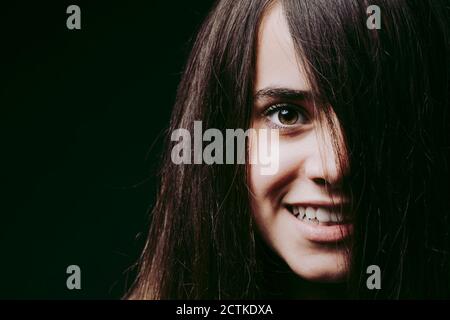 Close-up of smiling girl with brown hair on face against black background Stock Photo