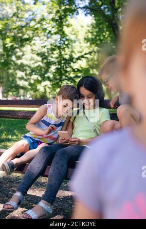 Girl with headphones showing technology to friends over bench in park Stock Photo