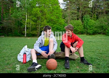 Two boys talking while sitting on log in forest Stock Photo