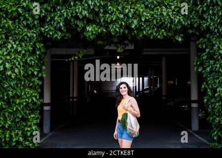 Smiling beautiful woman with reusable mesh bag standing at parking garage entrance Stock Photo