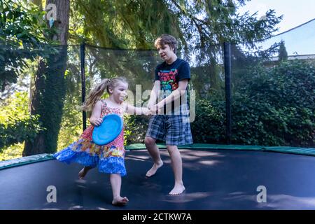 3 year old girl and her 17 year old brother playing on their trampoline Stock Photo