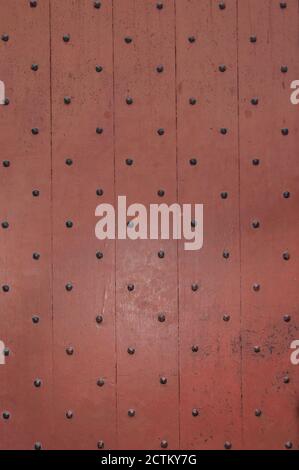 Old wooden door painted a muted red, with decorative black nail heads. Background texture or backdrop. Stock Photo