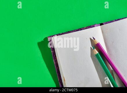 Opened notebook with purple and green pencils on green background , textured notebook pages Stock Photo