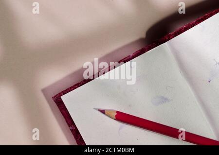 Opened notebook with red colored pencil , beautiful shadows on table , textured notebook pages Stock Photo