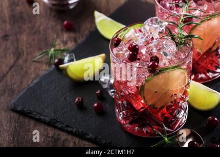 Glasses of cranberry drink or cocktail with rosemary, cranberries, vodka and crushed ice on grey background, copper bar tools, copy space Stock Photo