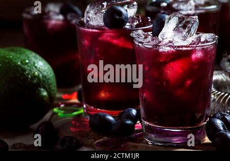 Alcoholic cocktail with liqueur, blueberry, lime juice, crushed ice, bar tools on black background, selective focus Stock Photo