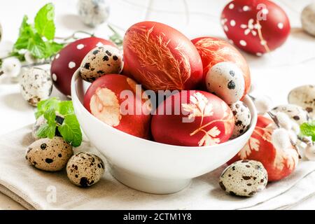 Painted brown Easter egg with a pattern, quail eggs, twigs of willow, mint leaves in a white porcelain bowl on an old white table in country style, se Stock Photo