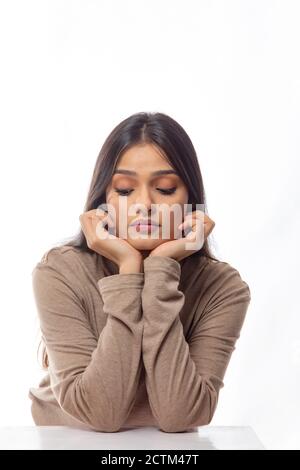 Young woman looking downwards with her face resting in her hands Stock Photo