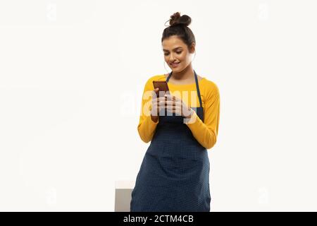 Woman in apron checking messages on phone Stock Photo