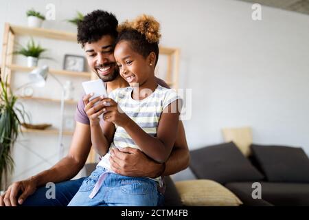 Happy father and daughter having fun with smartphone, smiling at funny video, playing mobile game Stock Photo