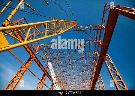 Construction of new factory building orange steel cstructure. Yellow girder crane and workers in construction suspended cradle. Wide-angle view. Stock Photo