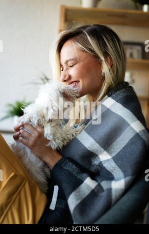 Beautiful woman playing with puppy on sofa at home Stock Photo