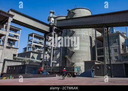 Mynaral/Kazakhstan - April 23 2012: Modern Jambyl Cement plant. Industrial buildings, cement silos, truck and worker on blue sky. Stock Photo