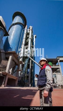 Mynaral/Kazakhstan - April 23 2012: Modern Jambyl Cement plant tower, silo, industrial building and  worker or engineer. Daylight on clear blue sky. Stock Photo
