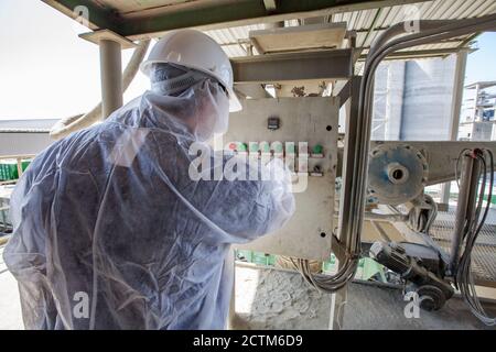 Mynaral/Kazakhstan - April 23 2012: Jambyl Cement plant. Engineer or worker in protective suit and white hard hat making an operation. Stock Photo