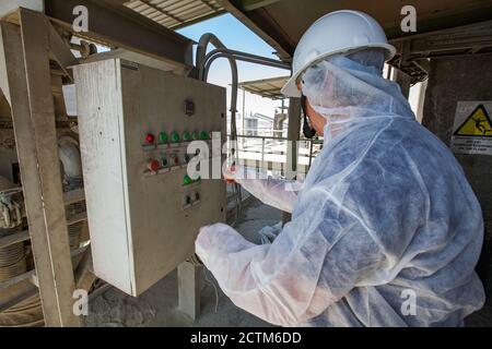 Mynaral/Kazakhstan - April 23 2012: Jambyl Cement plant. Engineer or worker in protective suit and breathe mask, white hard hat making an operation. Stock Photo