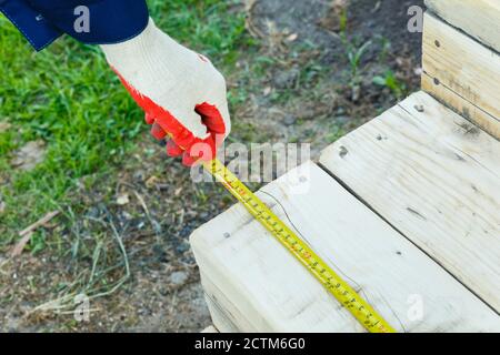 A man's hand holds a measuring tape and measures the length of the board. Measurement of the length of the building material. Stock Photo