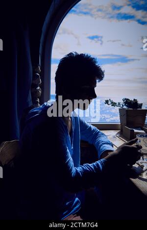 Silhouette of a young man finishing a cappuccino against the background of a window with a sea view. Stock Photo