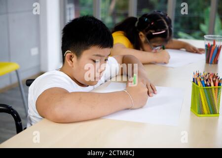 Asian disabled boy on wheelchair drawing picture with his friend in art class. Stock Photo