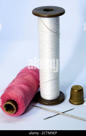 two spools of thread, two needles and a thimble on a light background Stock Photo