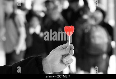 Outstretched hand offering a sign or symbol of love, care and compassion. Black and white background with isolated red colour love heart. Romantic Stock Photo