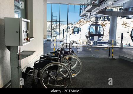 Many empty wheelchairs prepared for disabled people at station of cabin gondola ski lift at mountain alpine luxury austrian winter resort. Handicapped Stock Photo