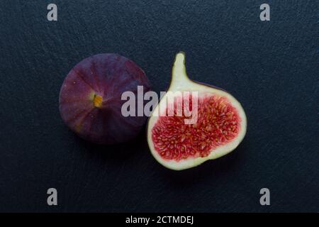 Two figs on black background. Whole figs and one fig sliced. Autumn dish. Fresh figs. Autumn harvest. Free space for text. Stock Photo