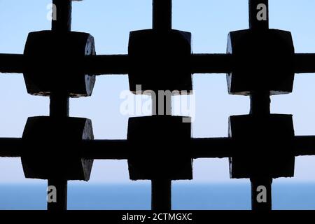 View through ancient metal lattice to sea and sky. Latticed window of medieval castle Stock Photo