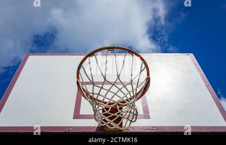 An old basket to play basketball on the background of a daytime bright cloudy sky Stock Photo