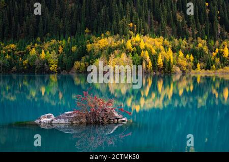 Mountain lake Issyk. Autumn mood. Yellowed trees are reflected in turquoise water Stock Photo