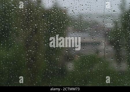 Raindrops on the glass, against the background of blurred green trees and buildings Stock Photo