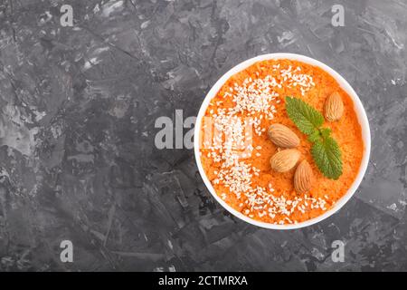 Carrot cream soup with sesame seeds and almonds in white bowl on a black concrete background. top view, flat lay, copy space. Stock Photo