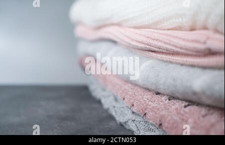 a pile of knitted sweaters in grey and pink colors. winter season clothes. selective focus. textured fabrics background. copy space for text or advertising. shallow depth of field. Stock Photo