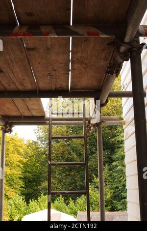 A view looking along through scaffolding between two old timber clad houses, one newly painted and one under repair and  awaiting painting Stock Photo