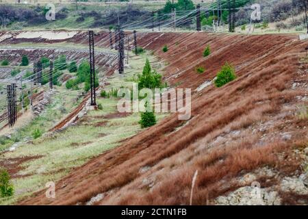 Giant iron ore quarry in Kazakhstan.  Mining raw minerals for metal production. Abandoned part of quarry with electric masts, grass and fir trees. Stock Photo