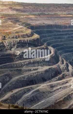 Giant iron ore quarry in Rudny, Kazakhstan. Open-pit mining raw minerals for steel production. Yellow quarry truck down. Quarry steps under beauty sun Stock Photo