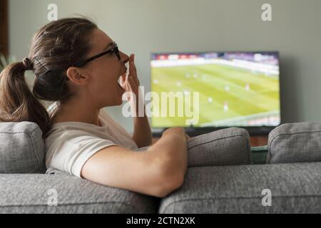Woman watching football on TV, she is bored and yawning Stock Photo