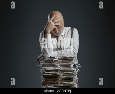 Pensive worried businessman leaning on a pile of paperwork, bureaucracy and administration concept Stock Photo