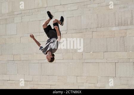 Upside down of young male doing somersault while practicing parkour in urban area in summer Stock Photo