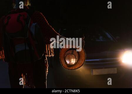 Back view of unrecognizable female hitchhiker standing on dark road and catching car at night during vacation Stock Photo