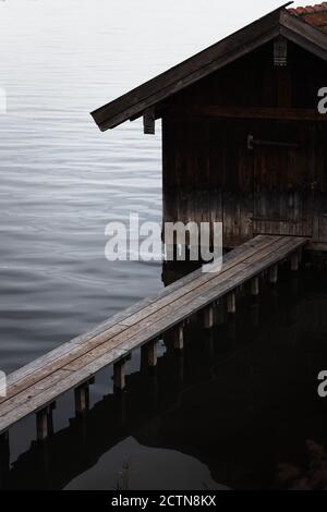 High angle view of weathered wooden boat shed and plank pier over rippling dark lake water in overcast weather in autumn day Stock Photo