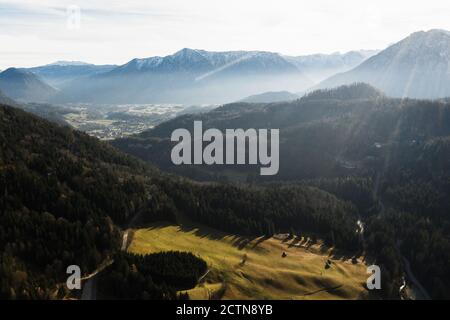 Spectacular aerial view of green valley with coniferous forest and mountain range with snowy peaks under shining sun rays Stock Photo