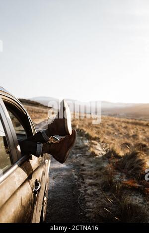 unrecognizable tourist lying in car with legs out of window on background of sunrise in Scottish Highlands Stock Photo